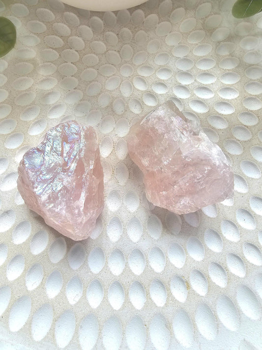 Two raw Aura Rose Quartz crystals displaying ethereal pink hues with iridescent rainbow flash, showcased on white textured surface